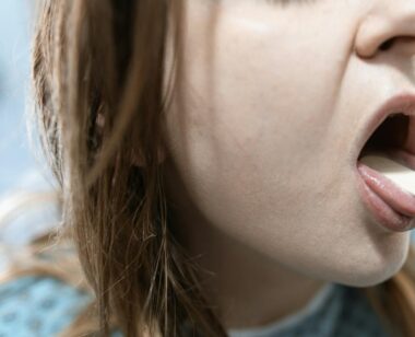 Close-up of a woman having her throat examined in a medical setting with a tongue depressor.